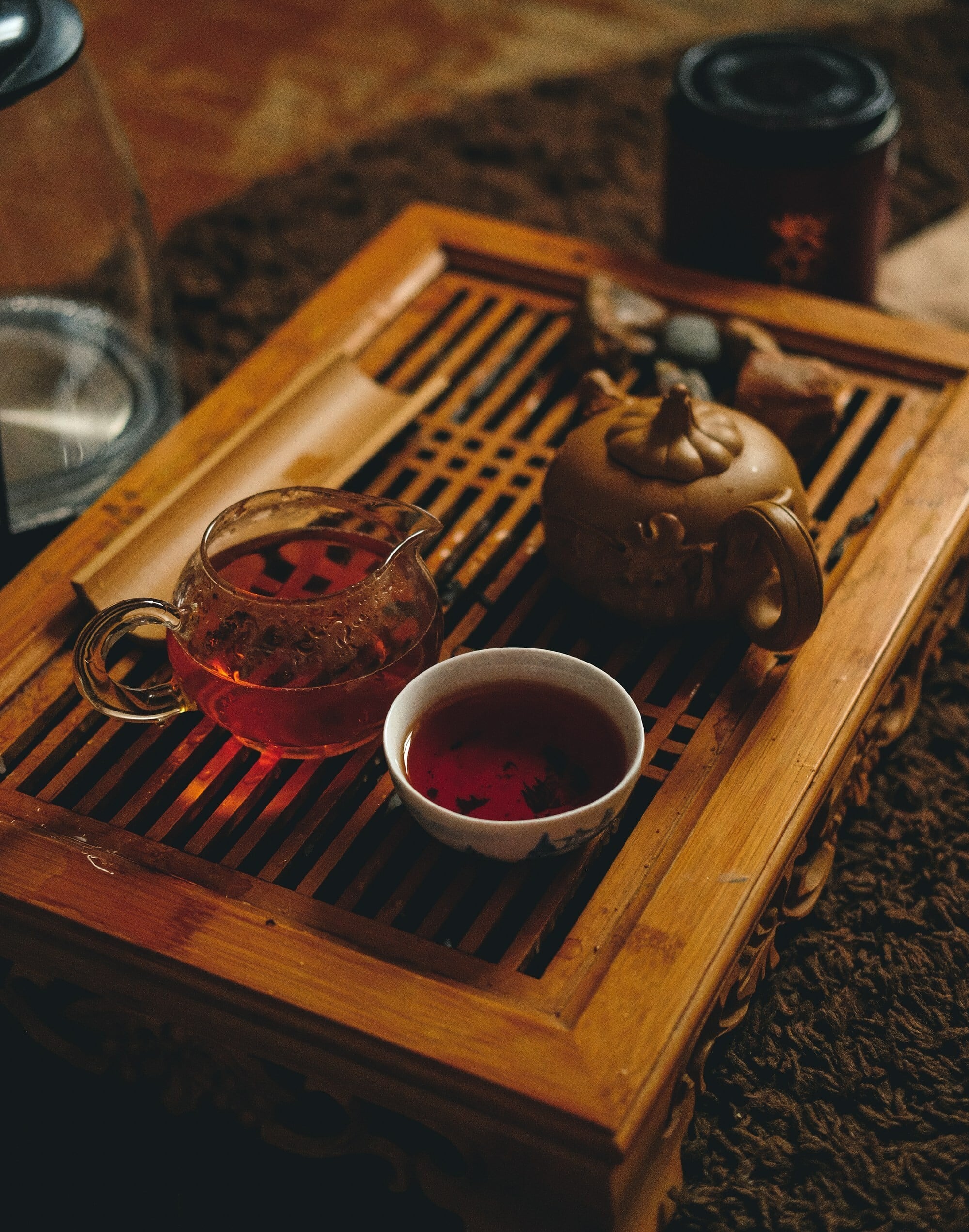 A wooden tray with a brass tea pot and a glass one with a tiny white cup